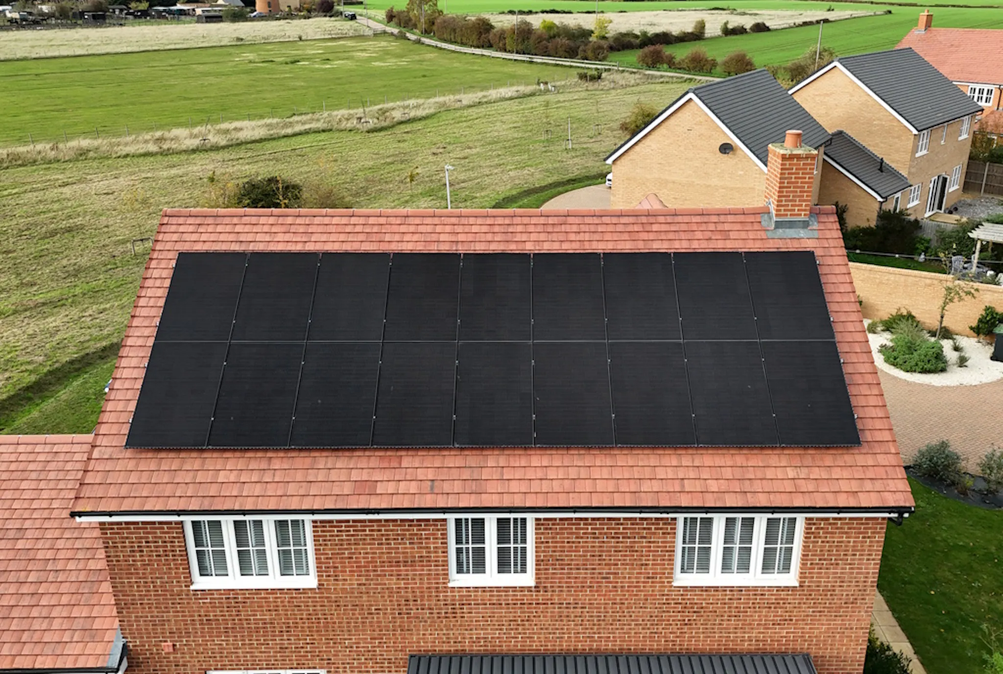 a house with a terracotta roof and black solar panels, against a green space