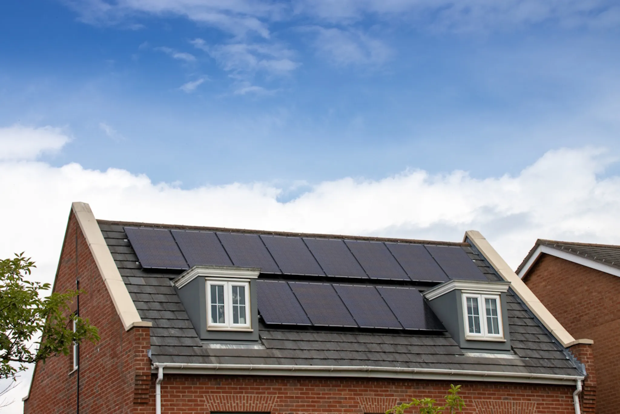 Eight black solar panels on a grey roof of a brick house, under a blue sky
