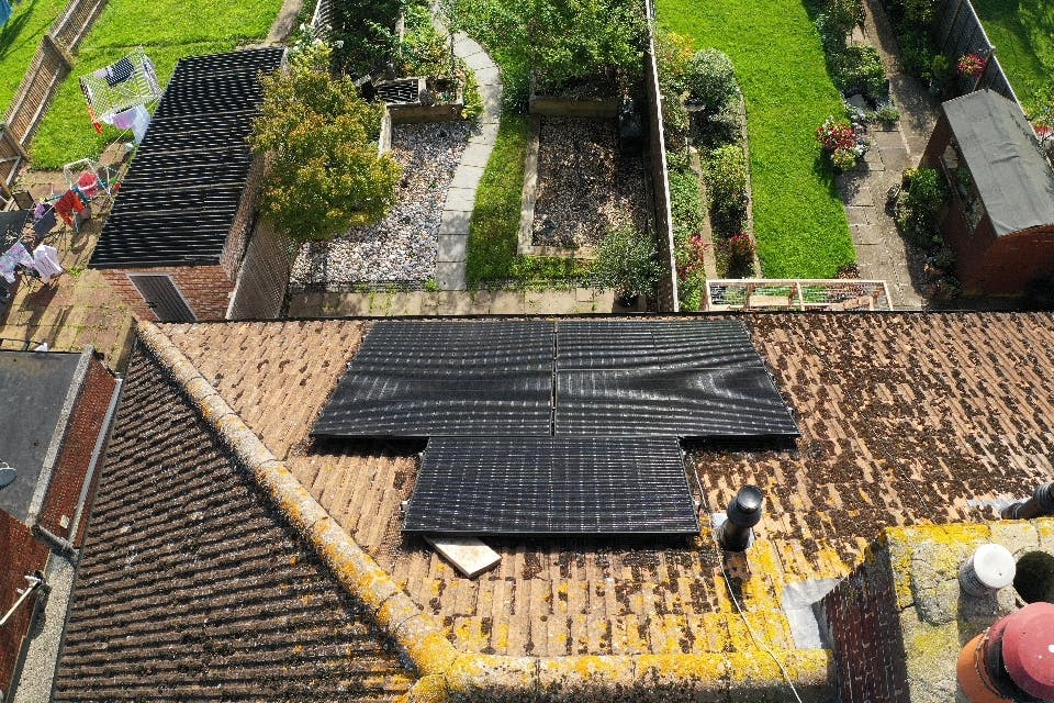 Black solar panels on a terracotta roof, overlooking green gardens lined with plants and trees