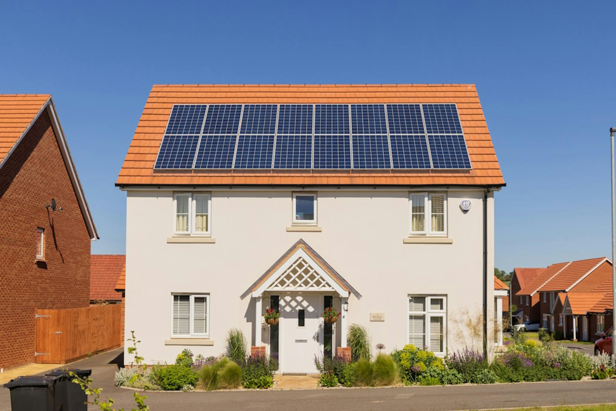 Detached house with solar panels on its terracotta roof, against a cloudless blue sky