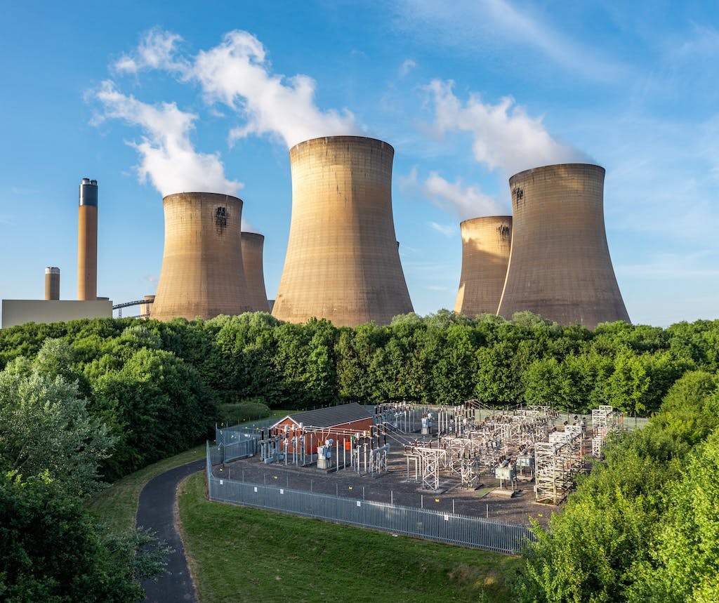 A gas-fired power plant in the UK, blue sky in background and trees in foreground