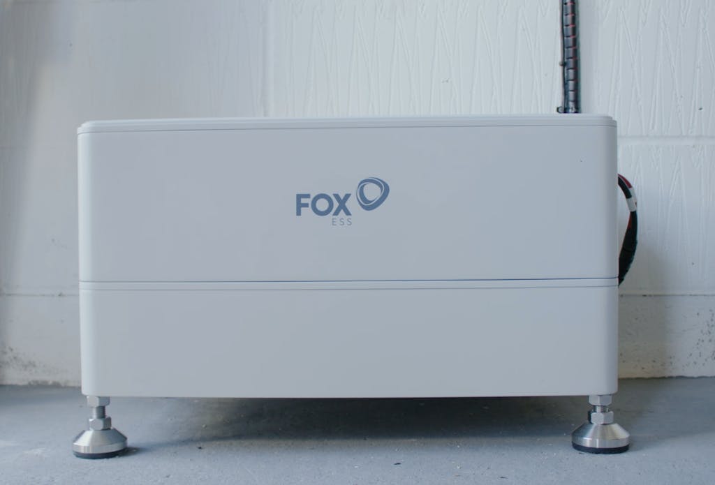 A white battery with 'FOX' written on it, on a grey floor, against a white wall
