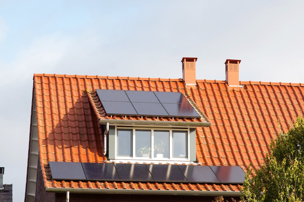 A terracotta-tiled roof with black solar panels on and below a dormer
