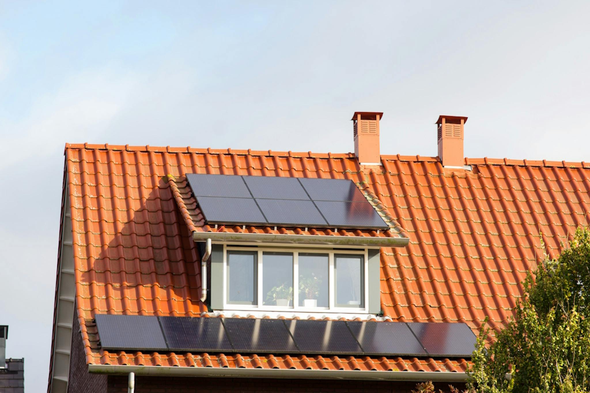 A terracotta-tiled roof with black solar panels on and below a dormer 