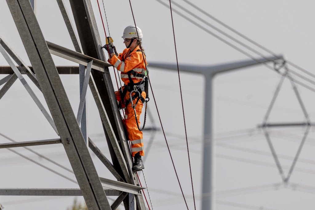 National Grid engineer in orange hi-vis clothing standing on an electricity pylon