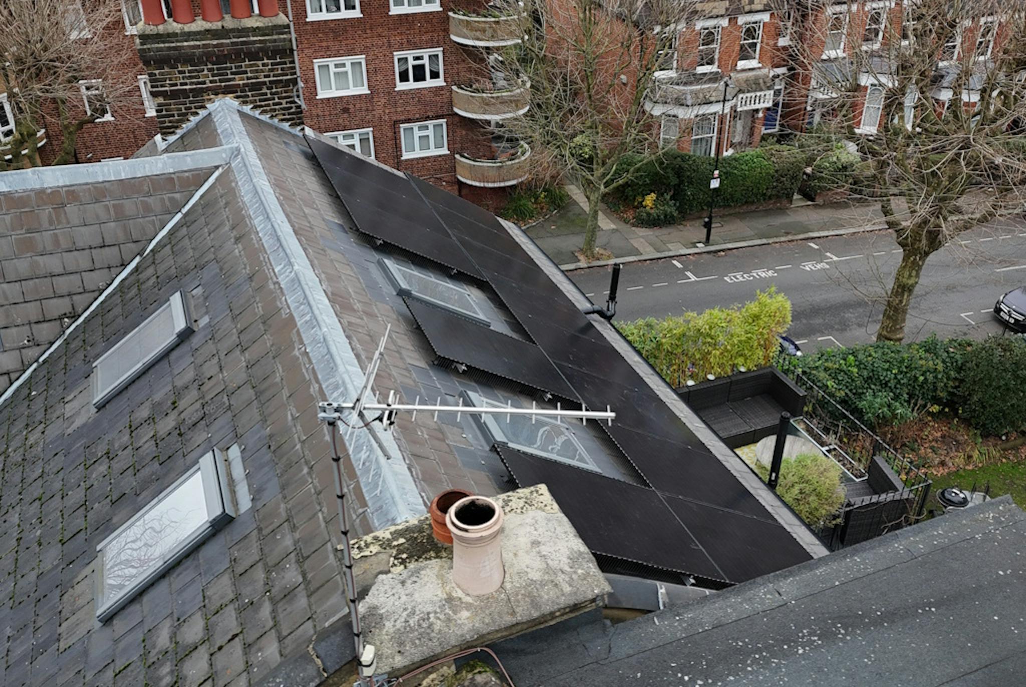 a grey roof with black solar panels and two skylights, against a backdrop of London homes