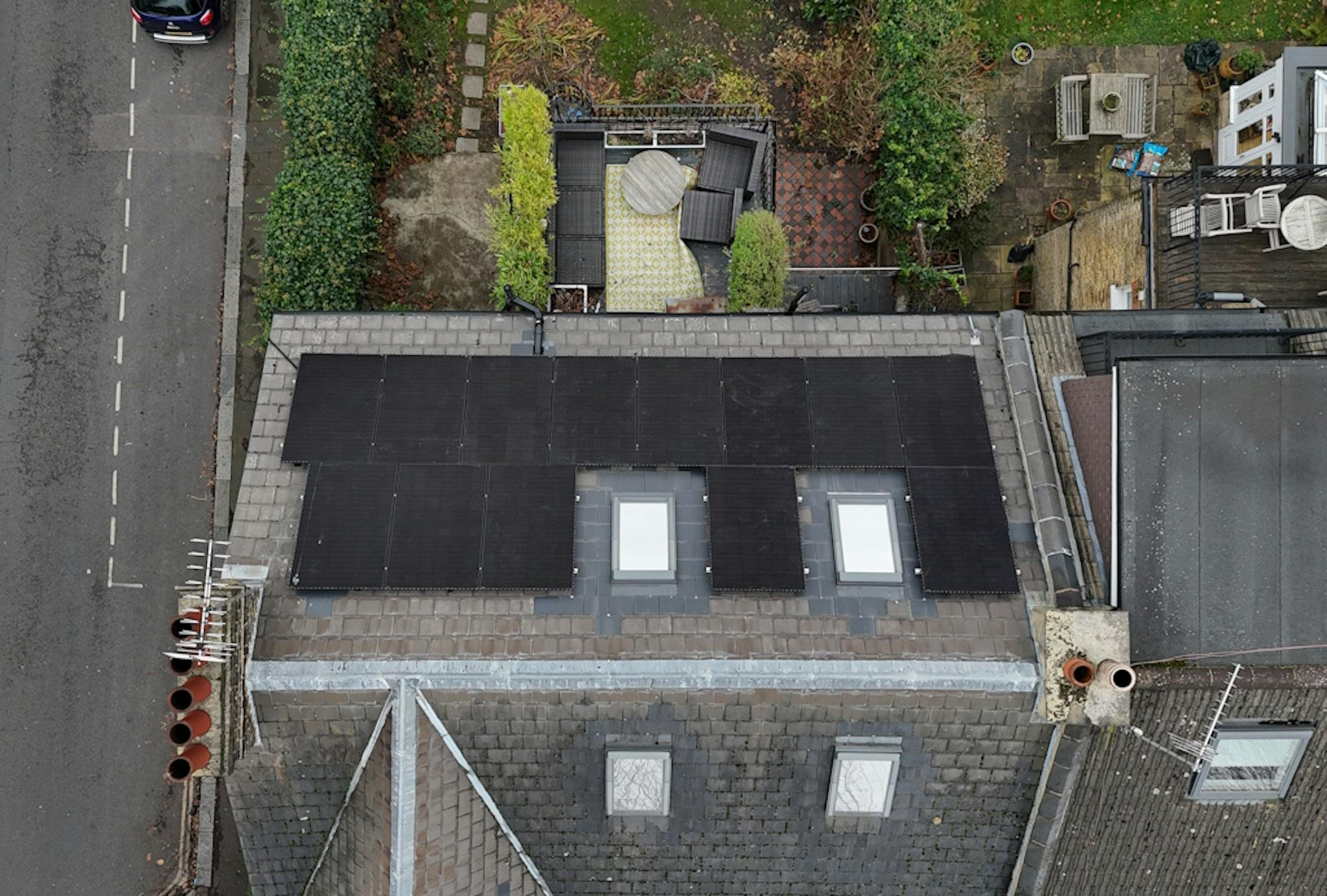 a grey roof with black solar panels and two skylights, against a backdrop of London homes