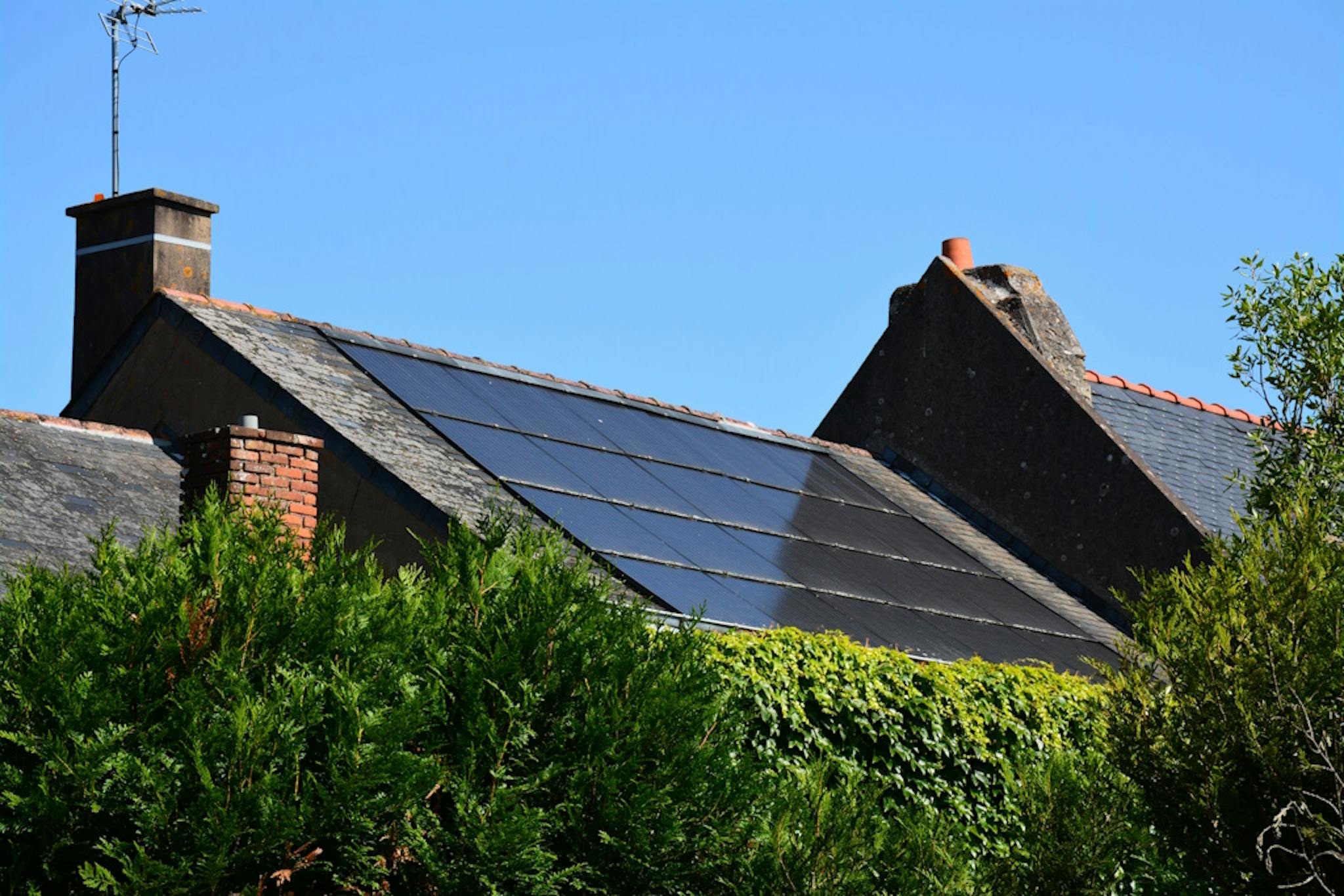 black solar panels on a grey roof, under a blue sky