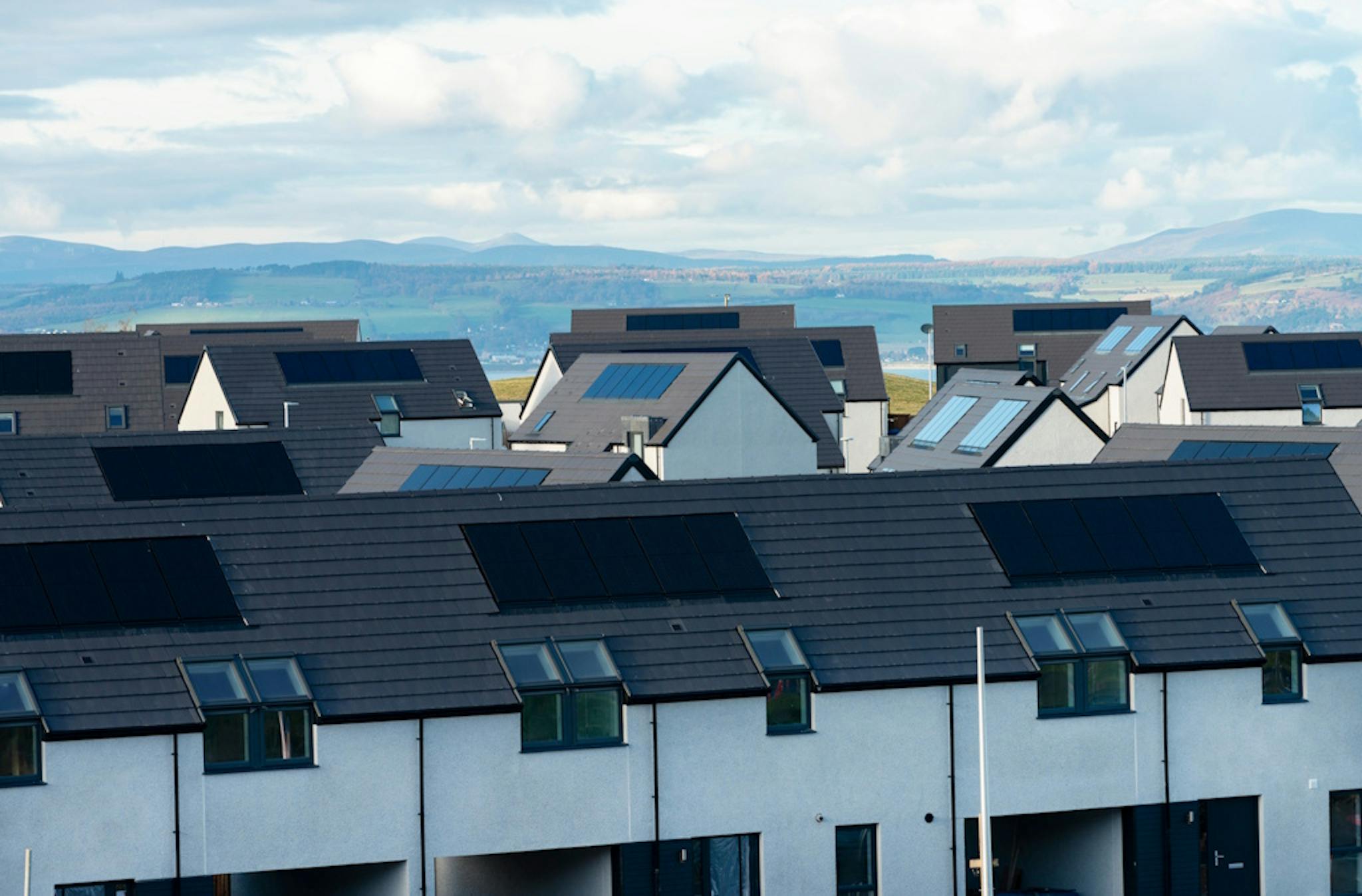 Houses with black solar panels on their roofs, against a backdrop of Scottish mountains