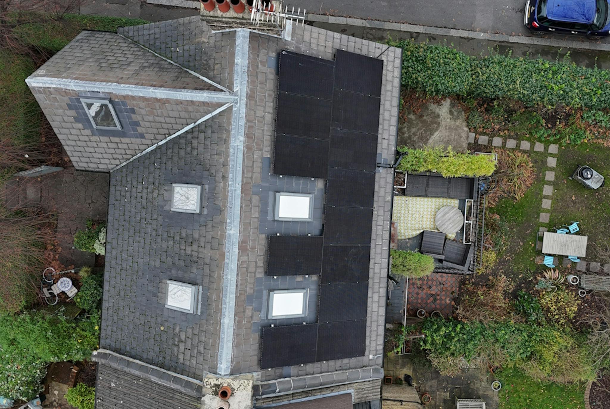 a grey roof with black solar panels and two skylights, next to a grey road