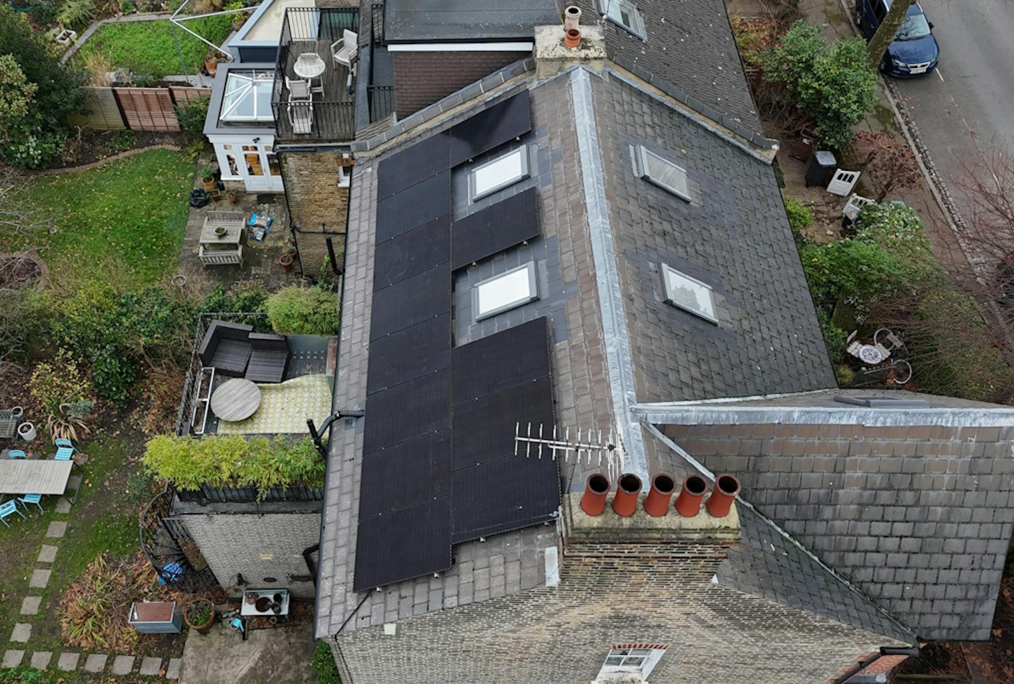 a grey roof with black solar panels and skylights, next to a grey road and a green garden