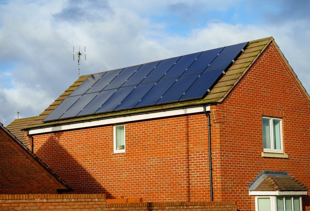 black solar panels on a brown roof, on a brick house, under a cloudy blue sky