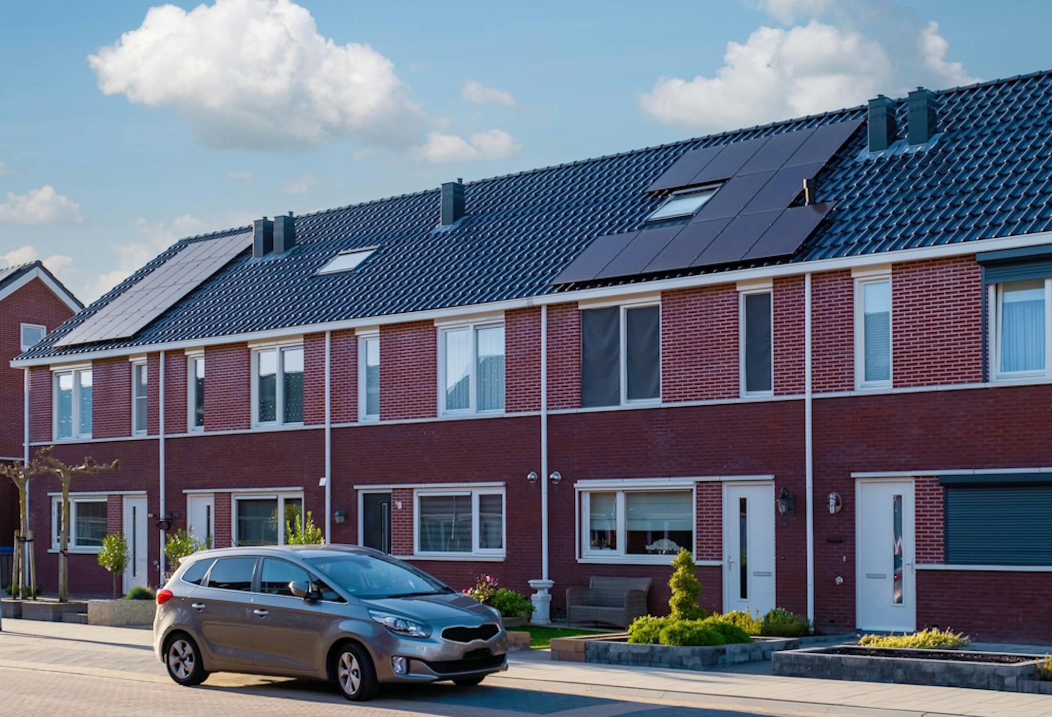 a grey roof with black solar panels and two skylights, next to a grey road
