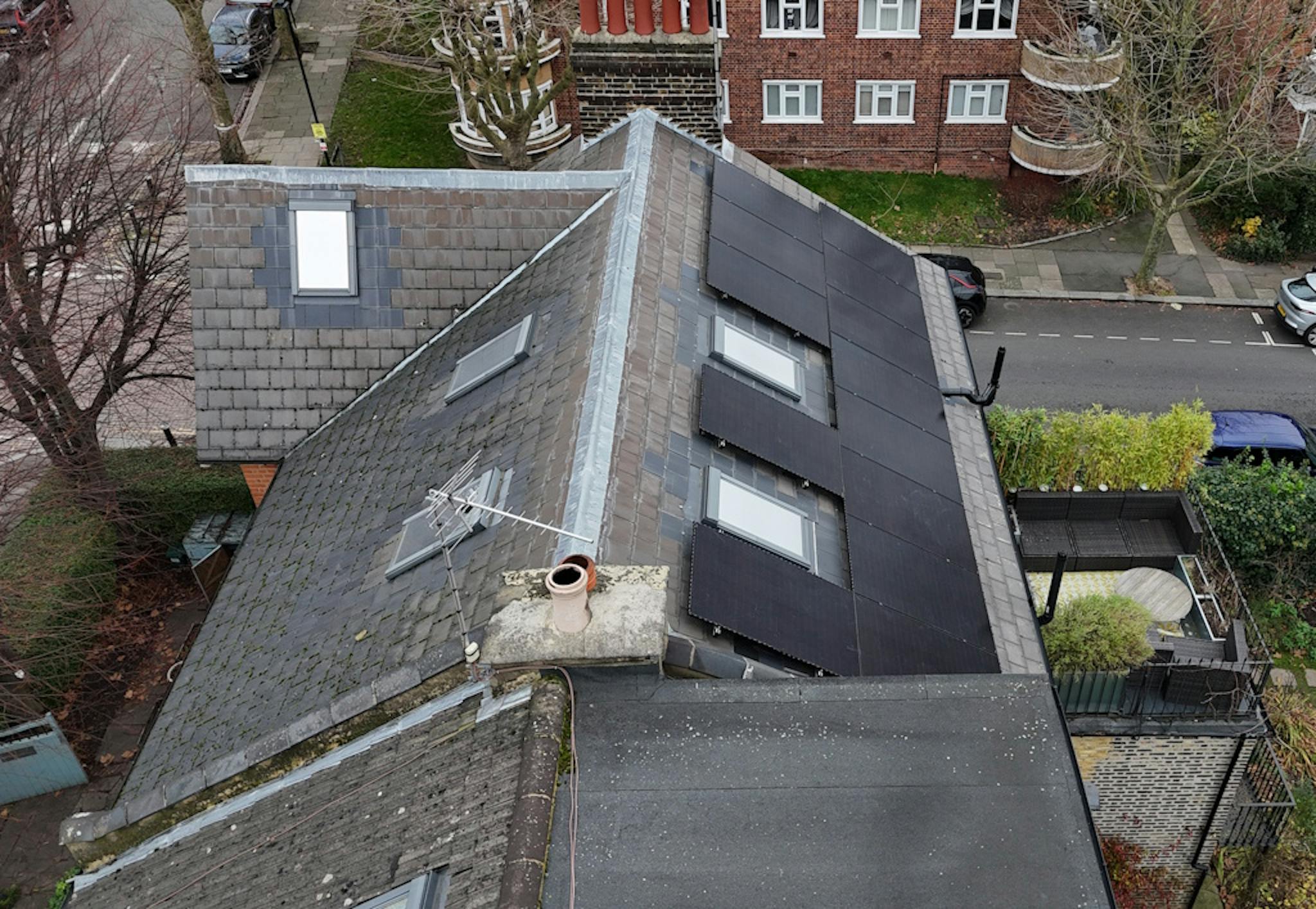 a grey roof with black solar panels and two skylights, next to a grey road