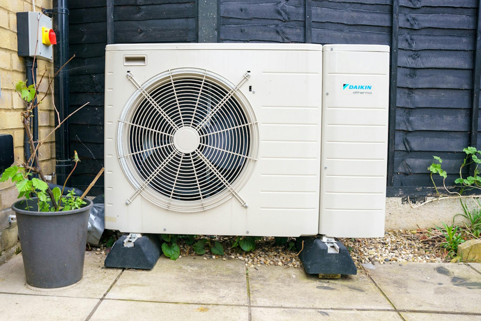 a heat pump on the ground by a wall, against a dark fence