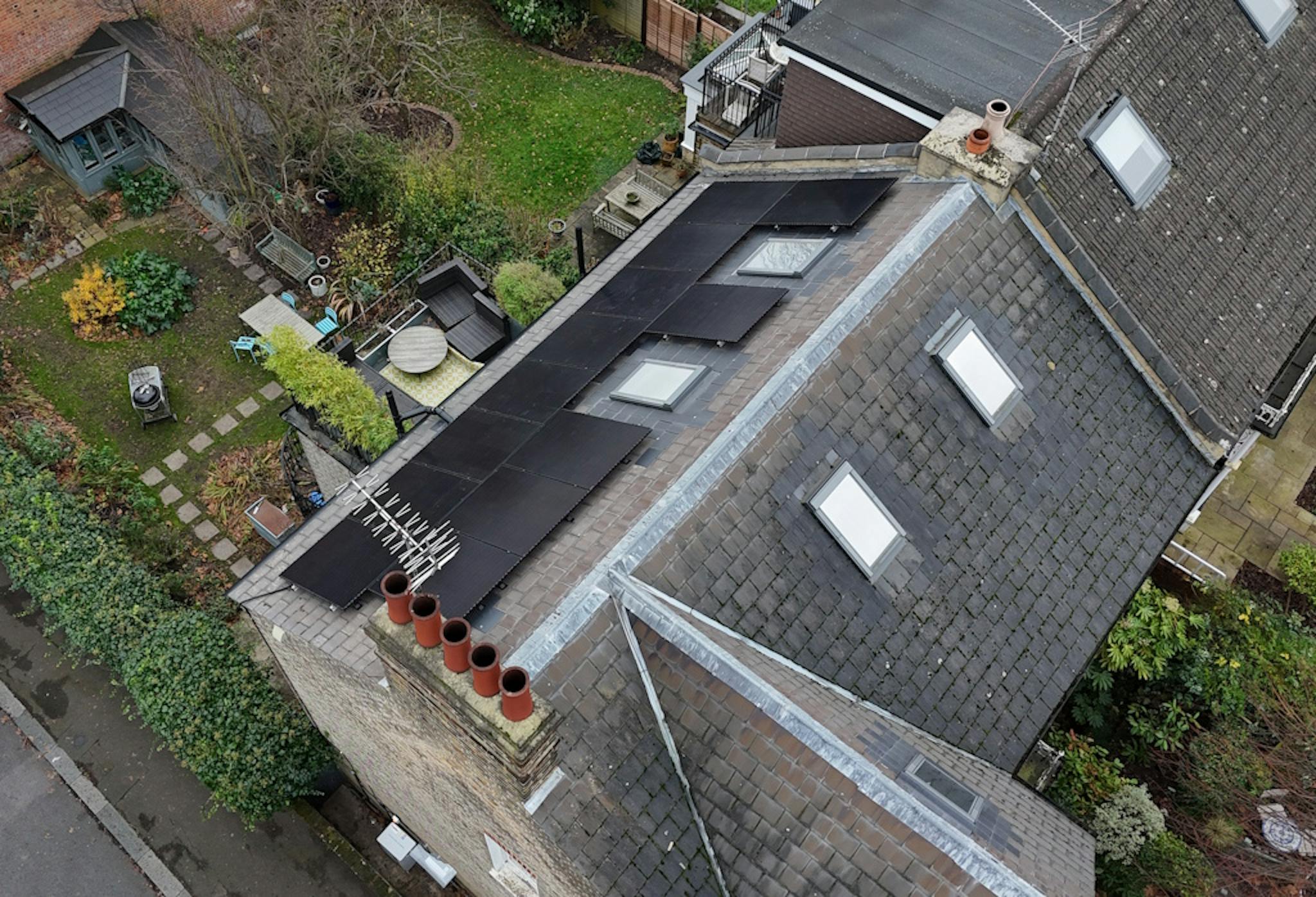 a grey roof with black solar panels and skylights, next to gardens