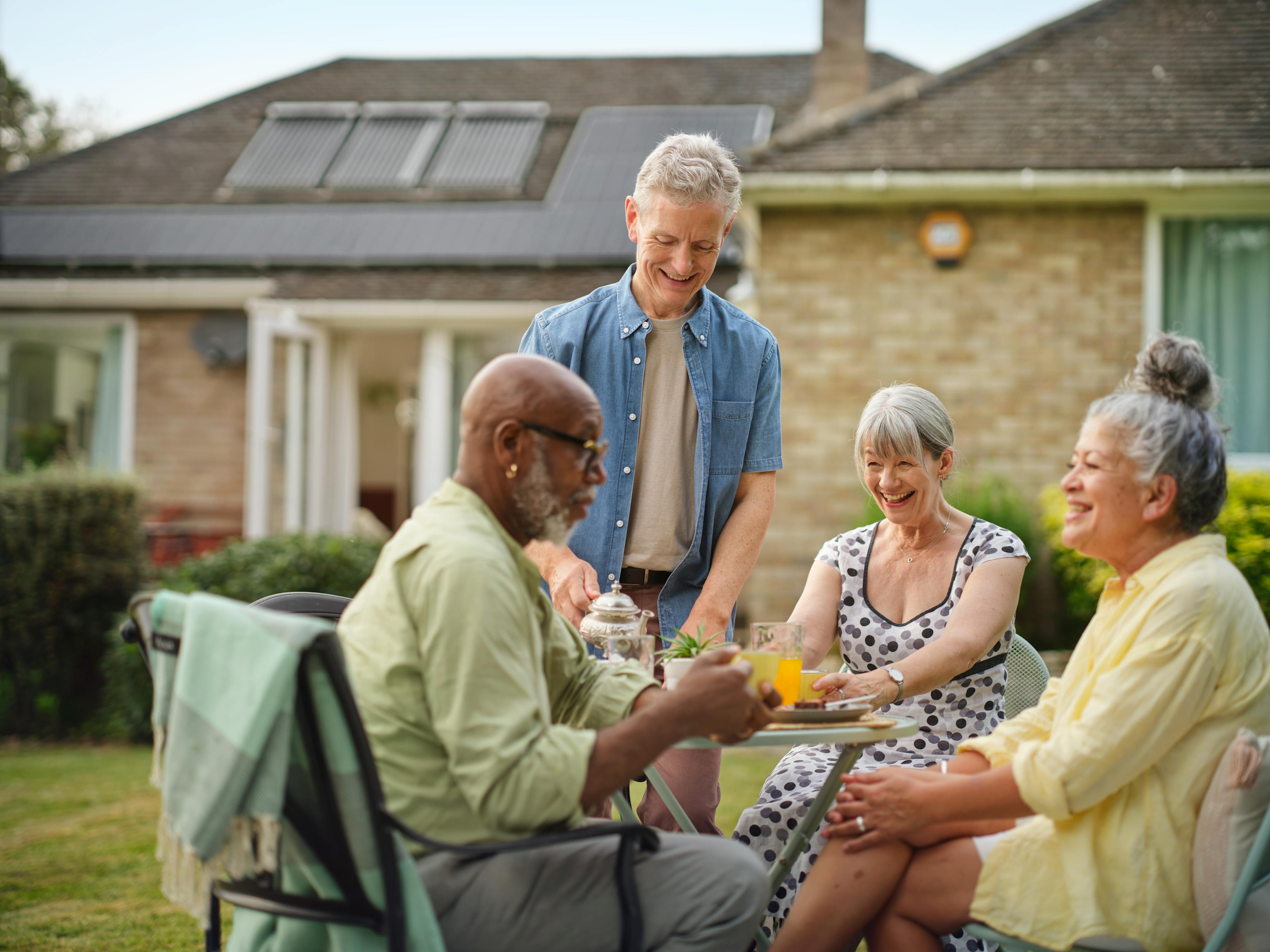 British gas image with four elderly persons enjoying a tea and snacks in the garden with background house equipped of solar panels