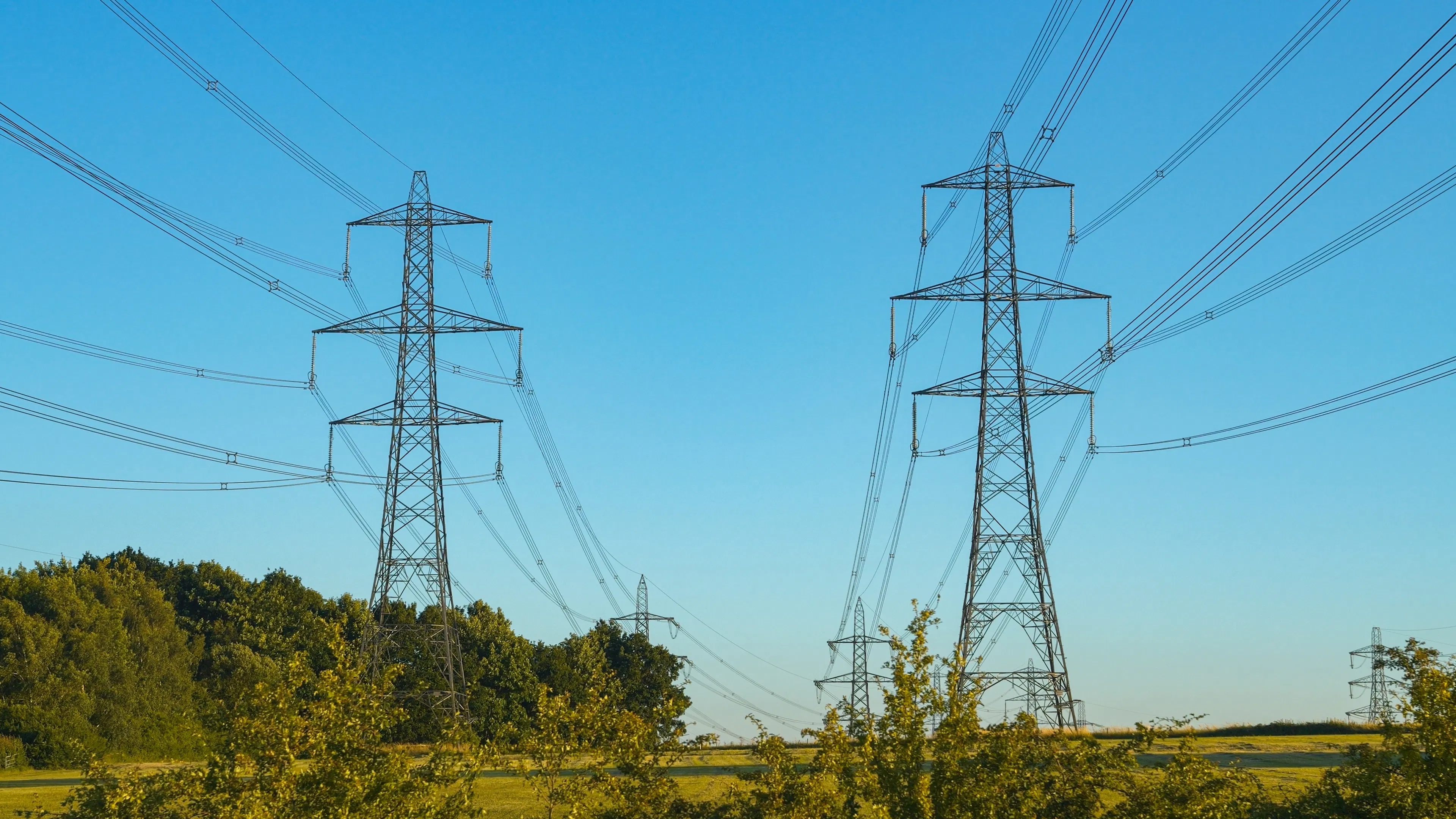 two high voltage transmission lines in UK countryside, blue sky in background