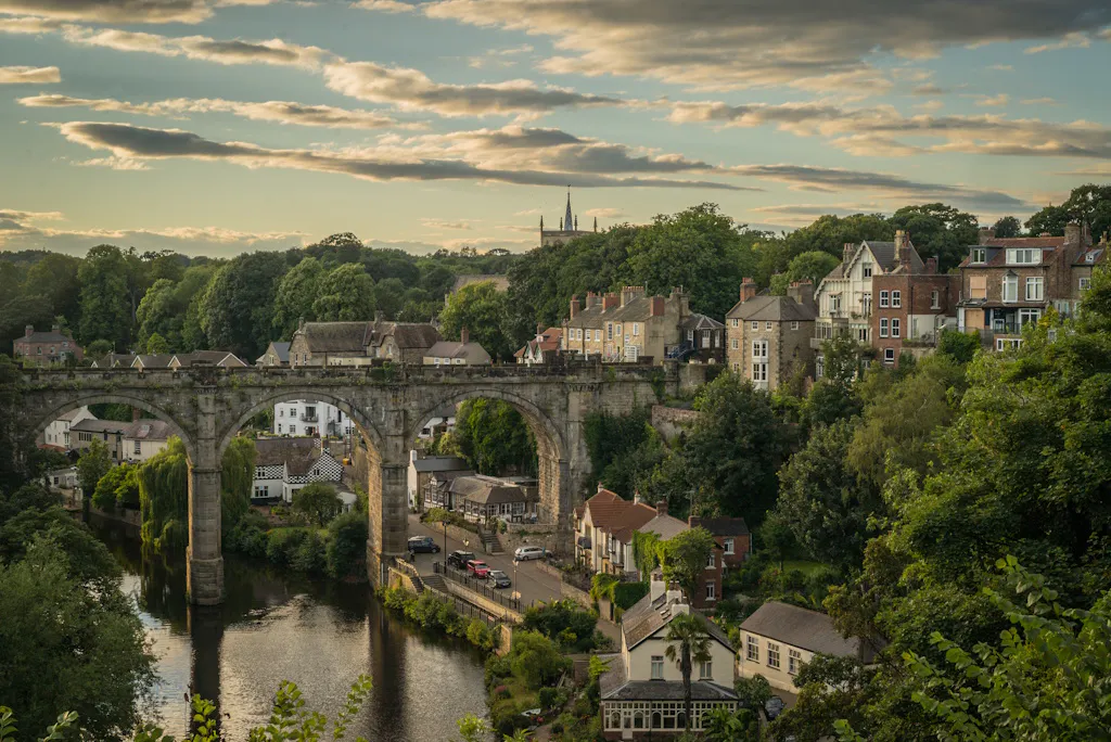 a bridge in Knaresborough, by some houses and trees, under a blue sky with clouds