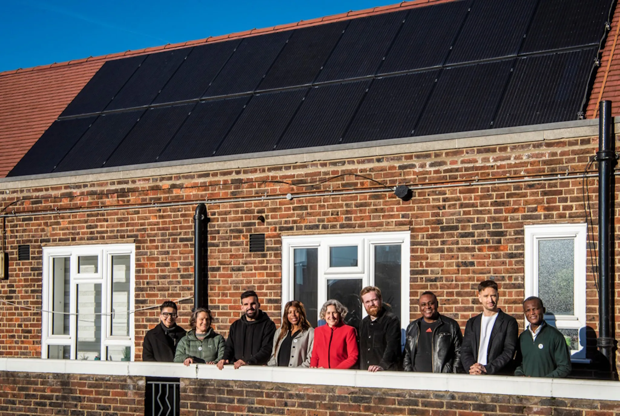 people standing in front of a black solar panel system on a terracotta rooftop