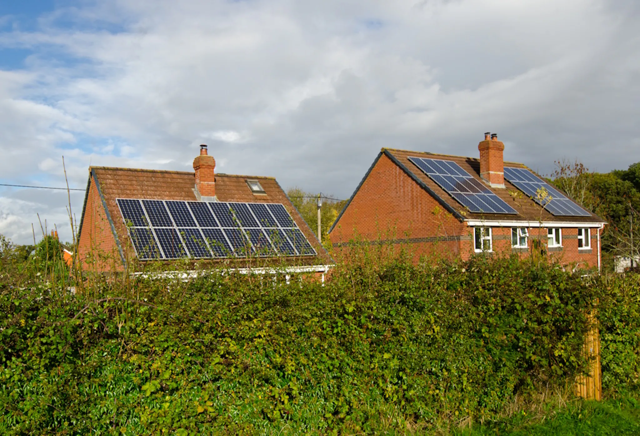 solar panels on two brick houses, under a cloudy sky