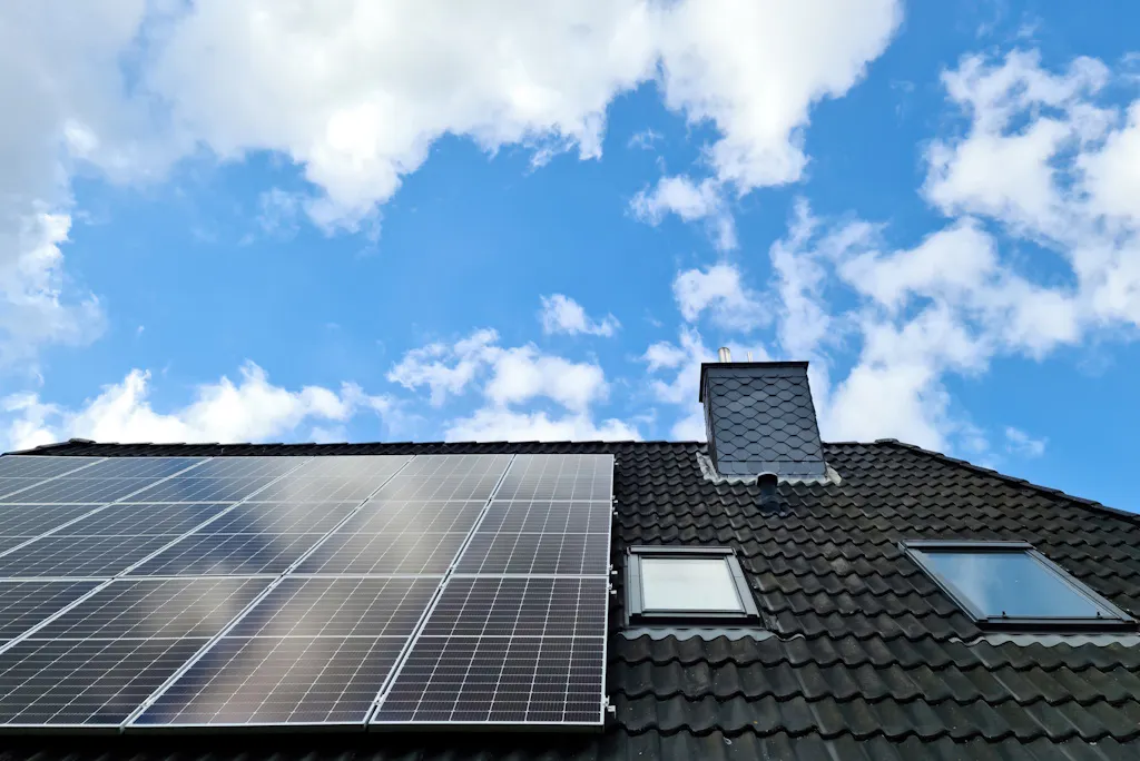 black solar panels on a roof by two Velux windows, under a blue sky