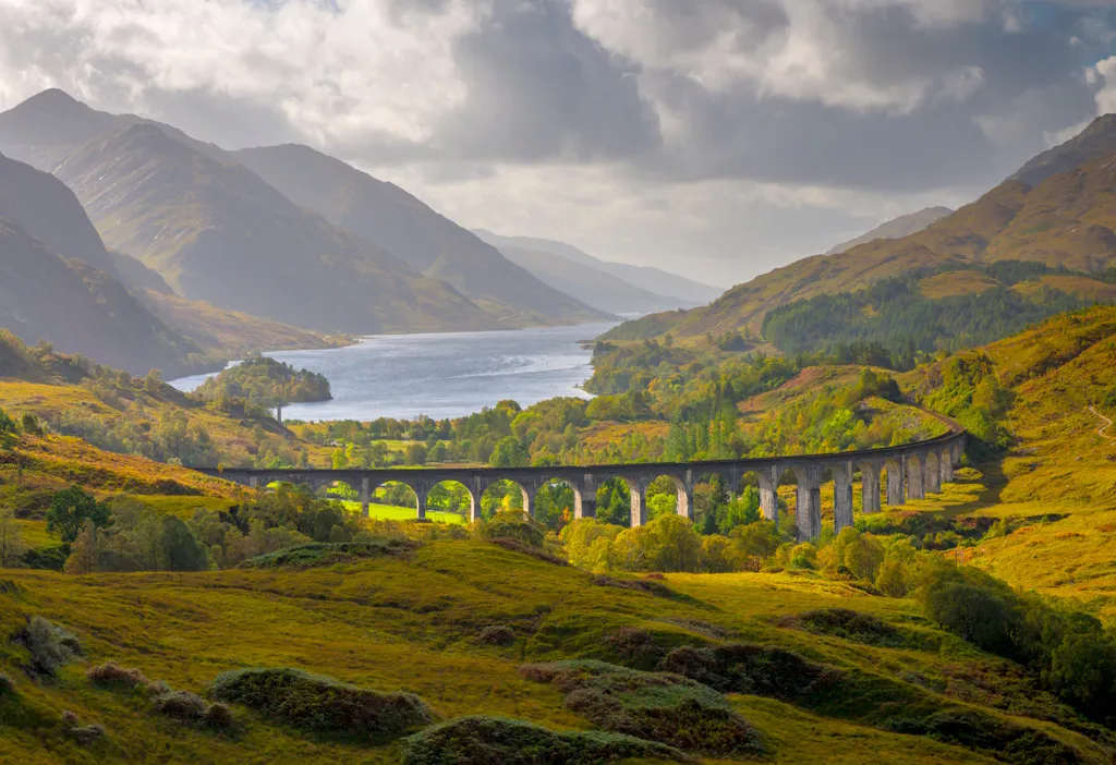 The Glenfinnan Viaduct, a railway viaduct in Lochaber, Scotland, against a backdrop of the sea, mountains, and fields