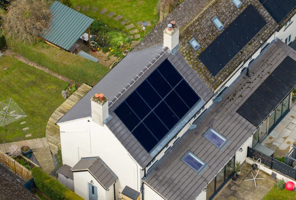 black solar panels on a grey roof, on a white house, next to a brown house with solar panels on the roof
