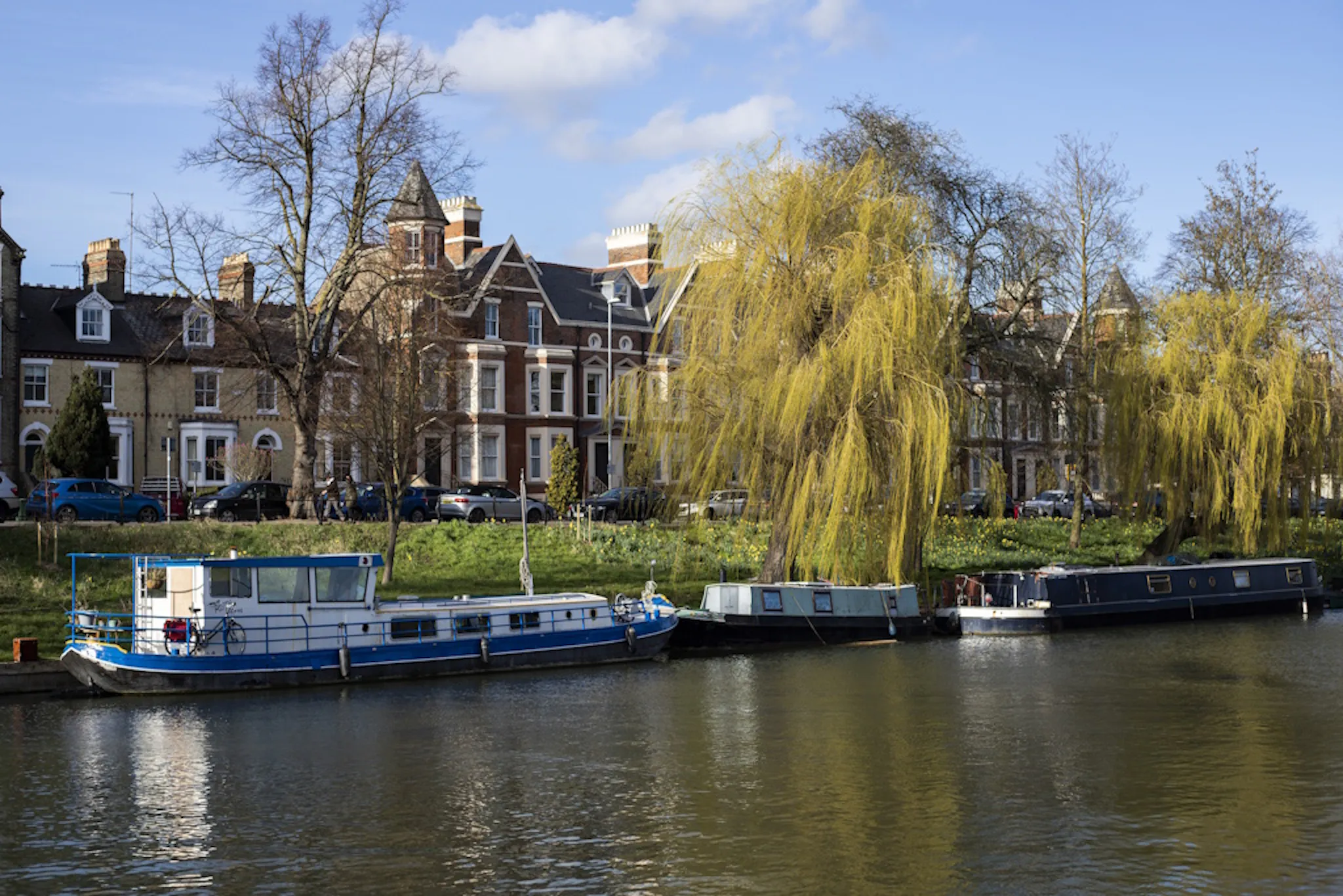 A river with a houseboat on it, against a series of houses, under a blue sky