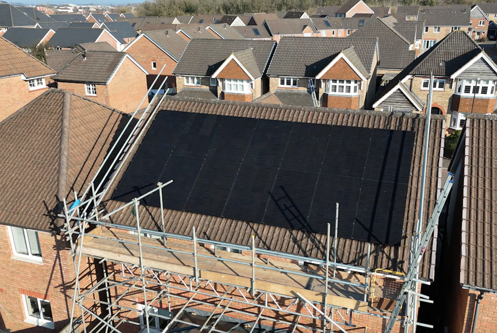 a house with scaffolding and black solar panels on the roof, surrounded by other, similar houses