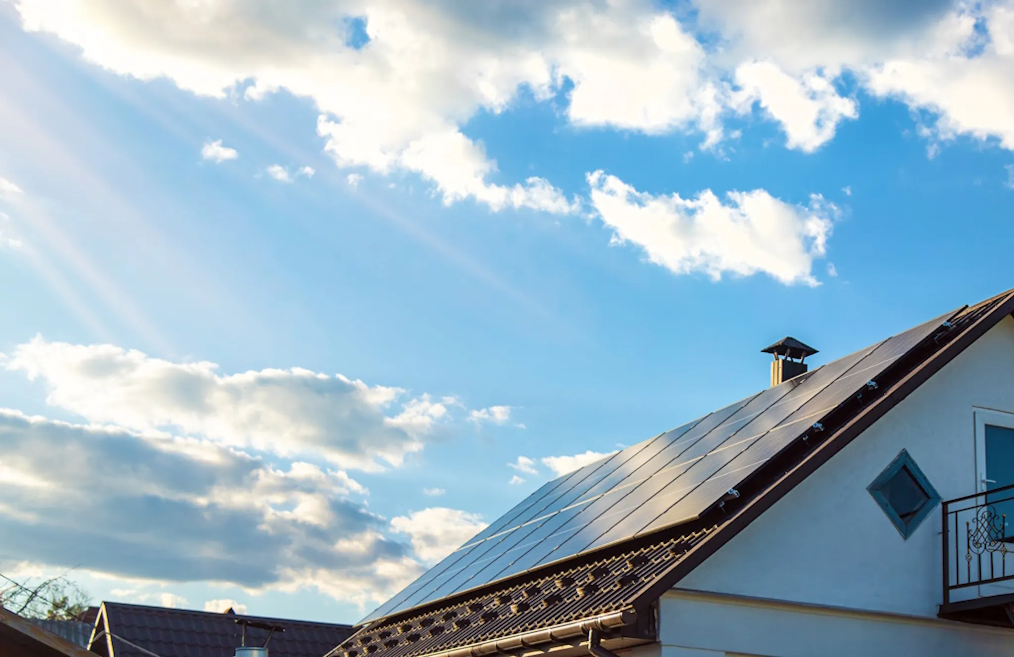 blue sky with clouds and the sun shining down on solar panels on a brown roof