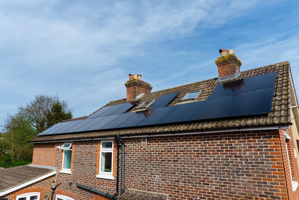 Black monocrystalline solar panel array on a rooftop in the UK, trees and blue sky in the background