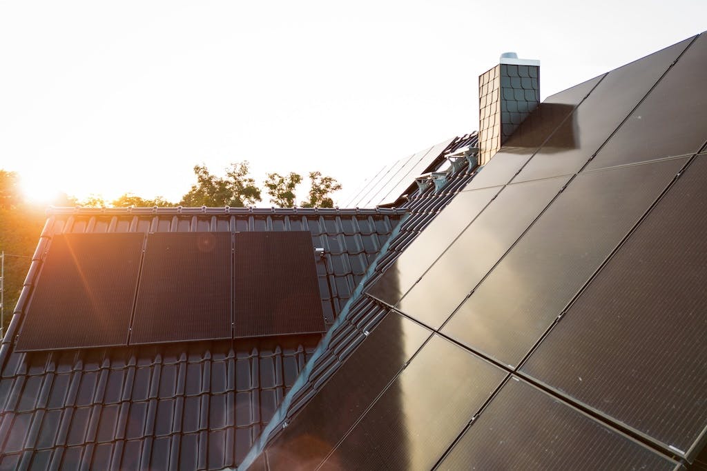 An array of black solar panels across two sides of a rooftop, with the sun rising above them