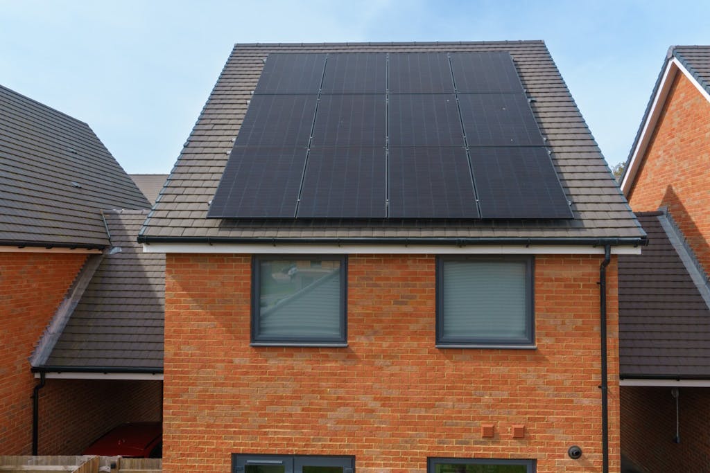 Photo of a brick house with black solar panels on a grey roof, under a light blue sky
