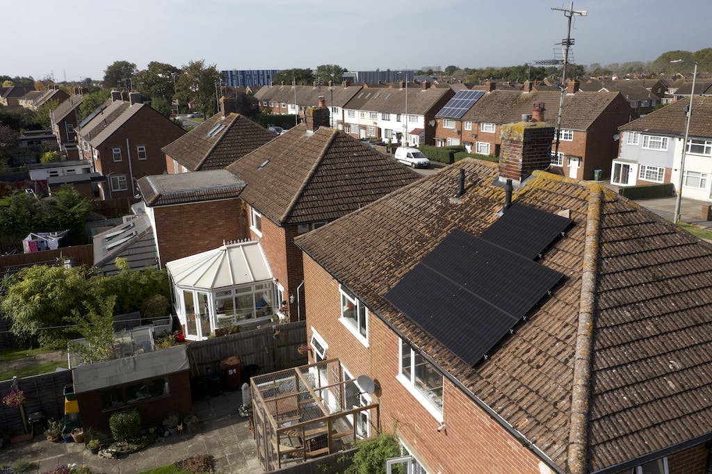 Black solar panel array on a brown rooftop in a UK neighbourhood, other houses in the background