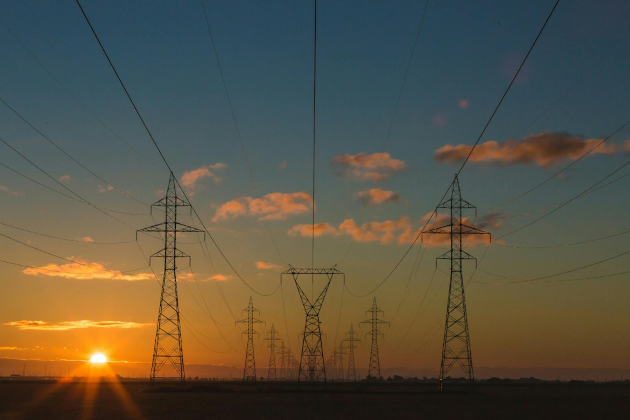 a landscape with a series of electricity pylons set against a sunset