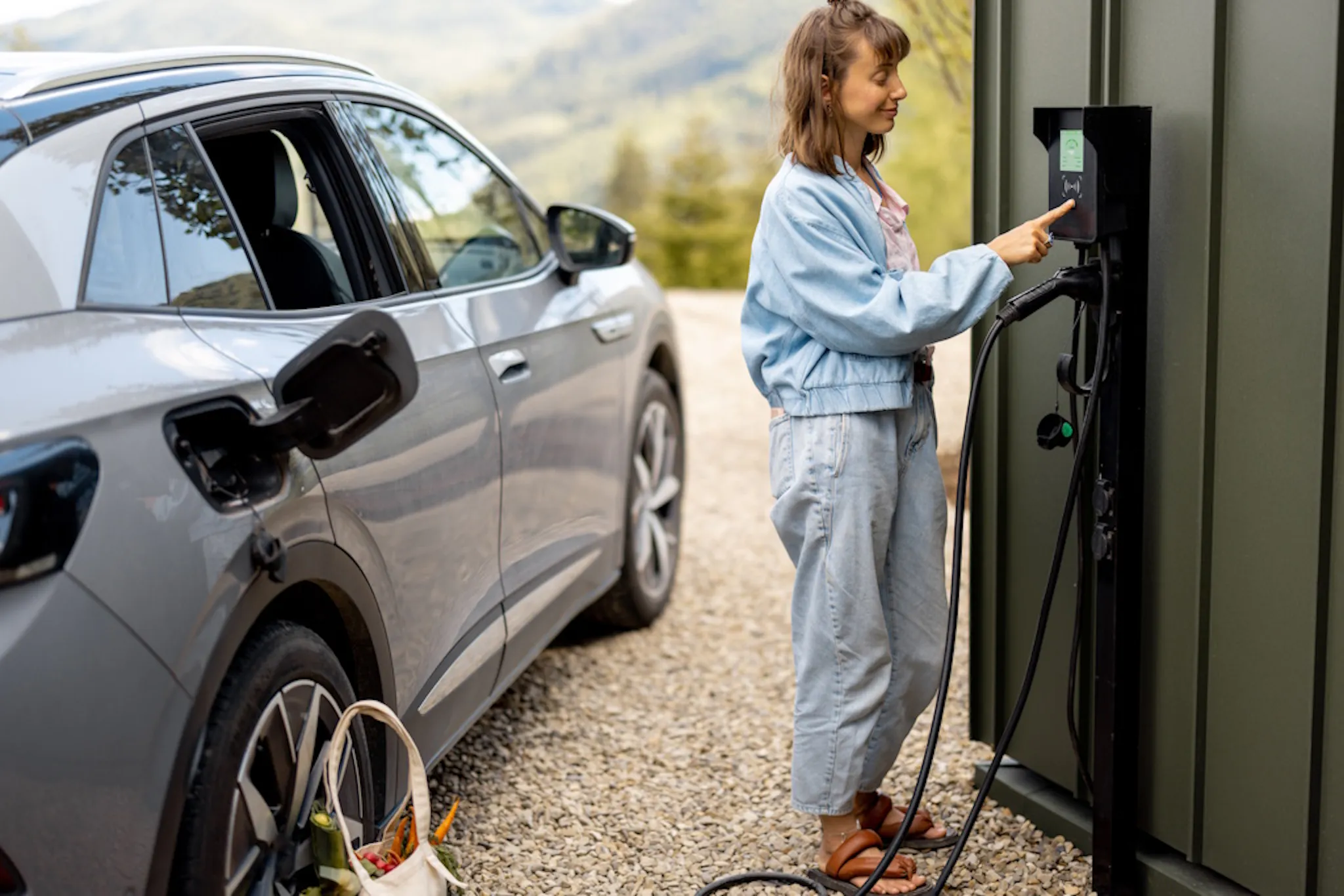 a person operating an EV charger, next to their silver car