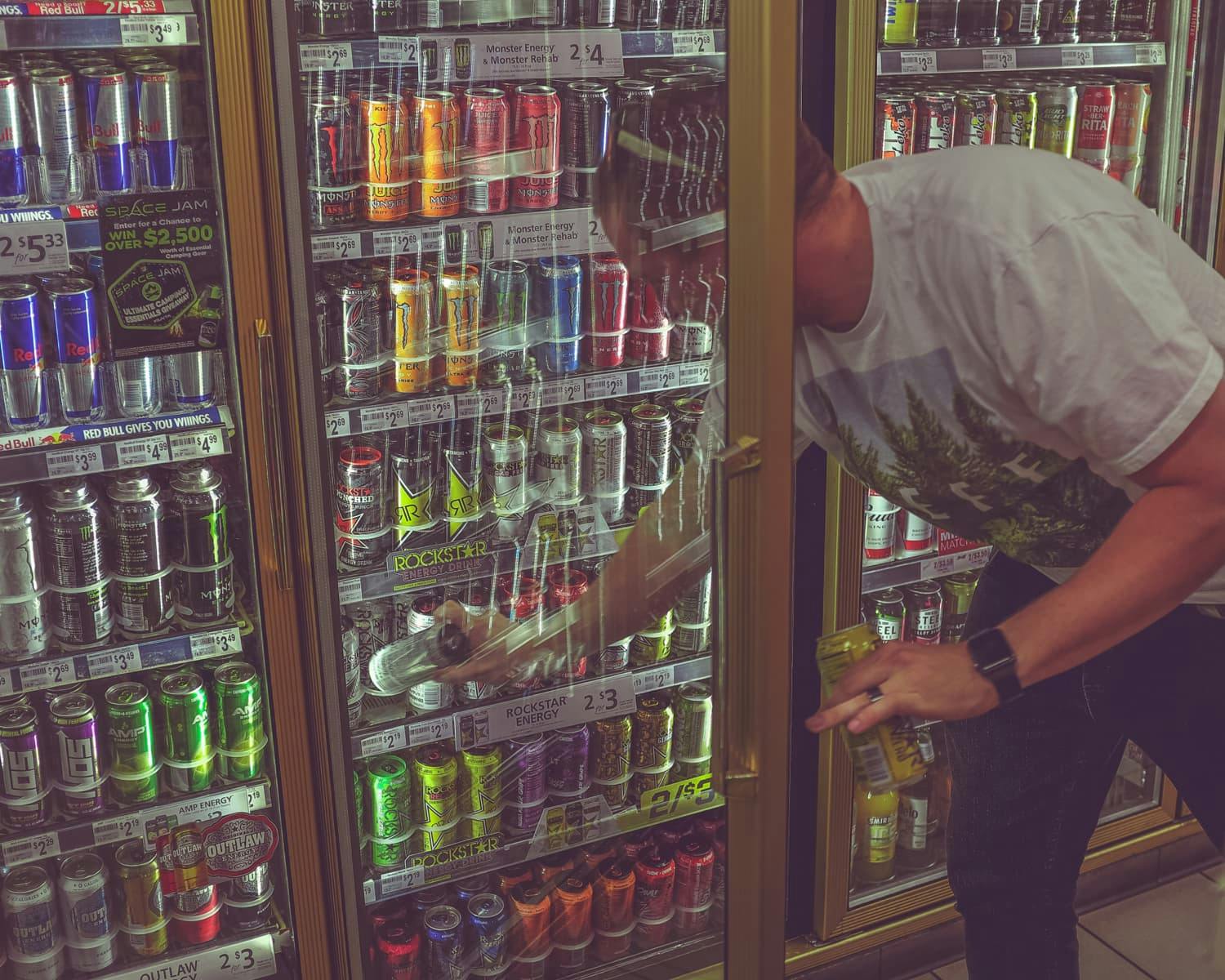 Man taking can of energy drink from store fridge.