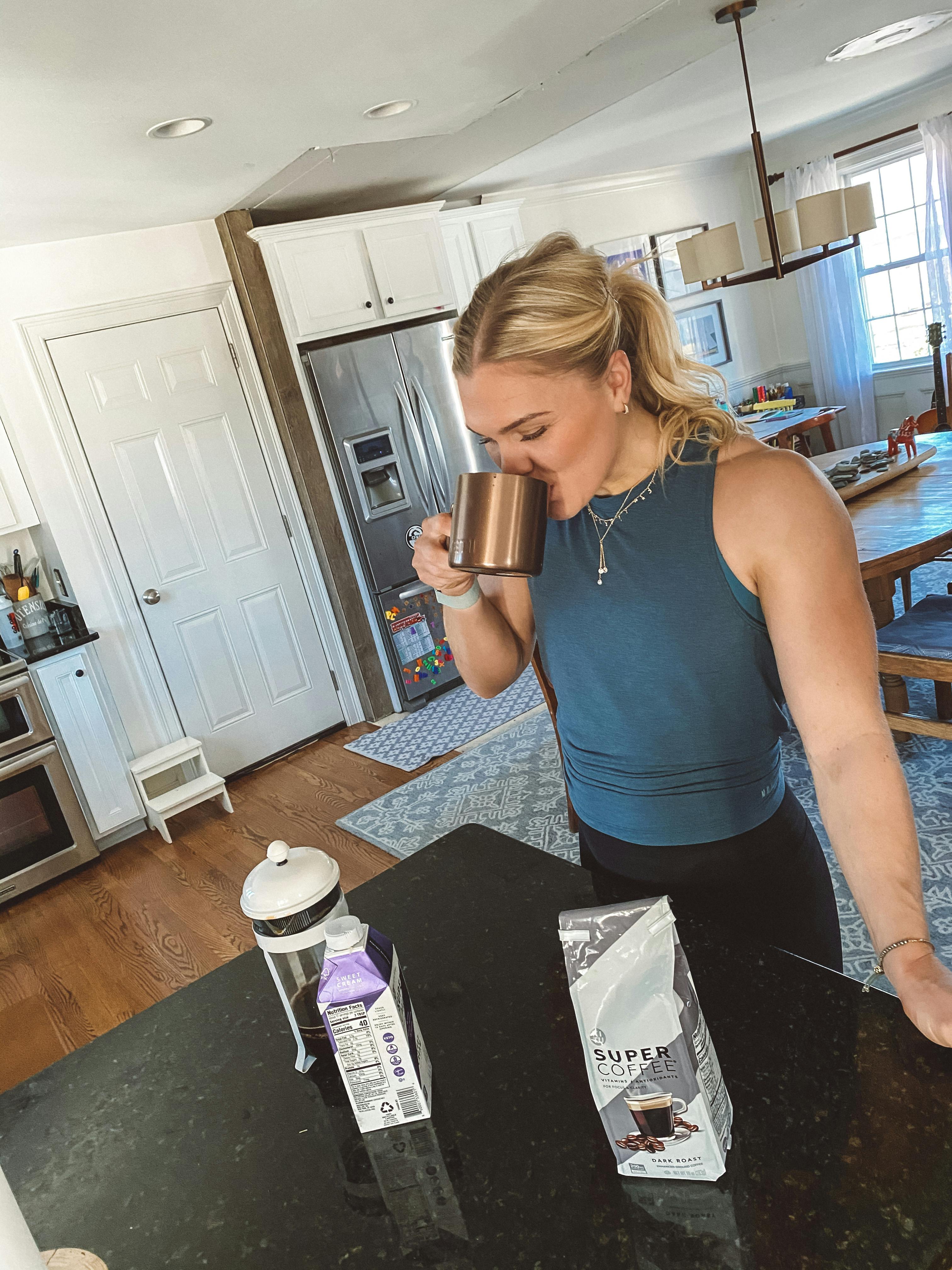 Katrin with a french press coffee maker, sipping on coffee at home.