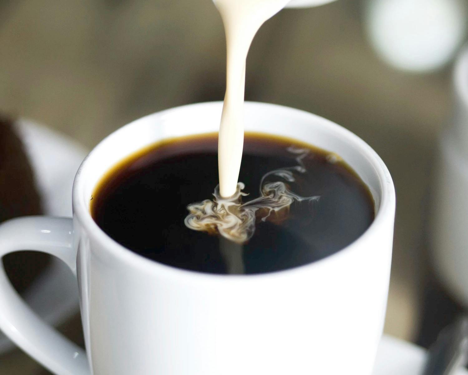 Coffee creamer being poured into a cup of coffee.