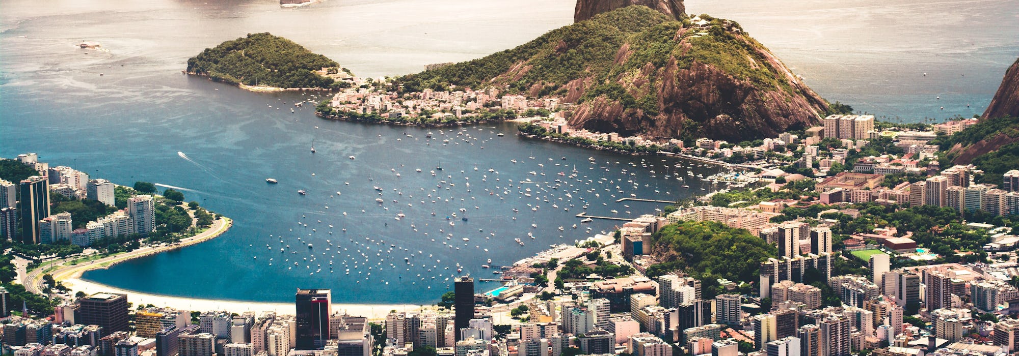 Foto på Rio de Janeiro från ovan med byggnader, berg och kristallblått vatten.