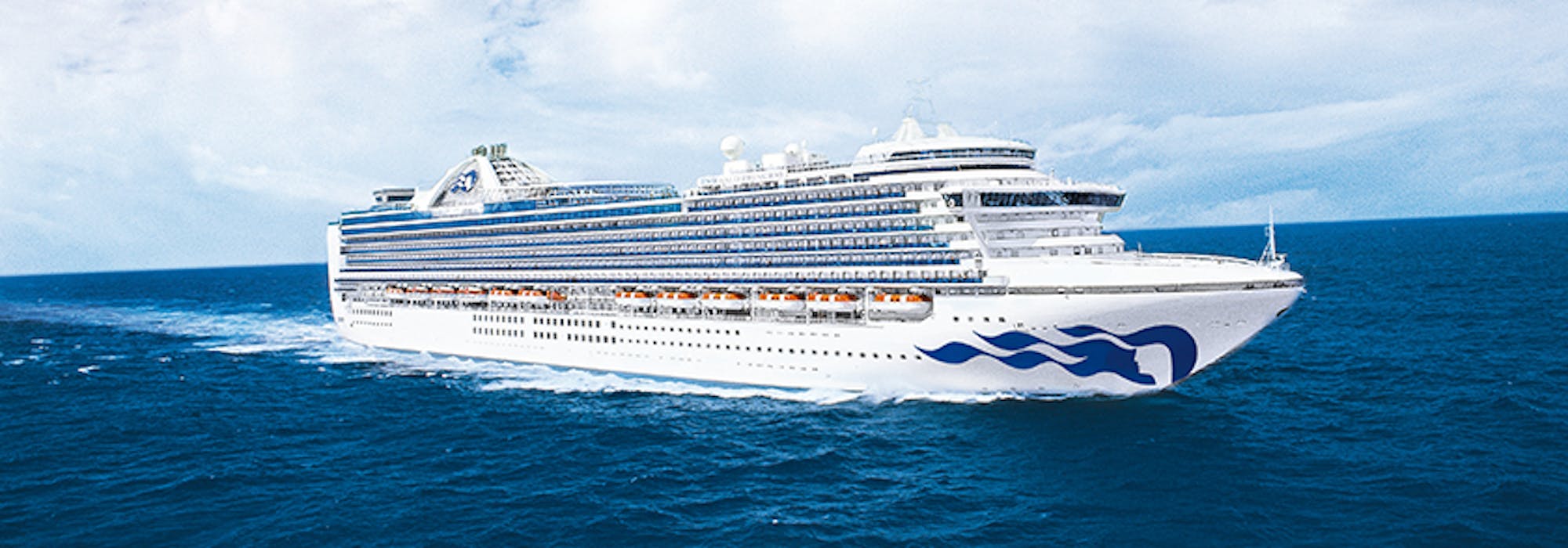 Bild tagen från sidan medan fartyget Emerald Princess kryssar fram i blått vatten.