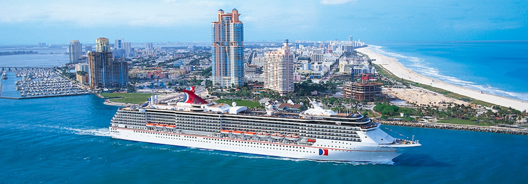 Carnival Pride kryssar förbi en stor ö med sandstrand och byggnader.