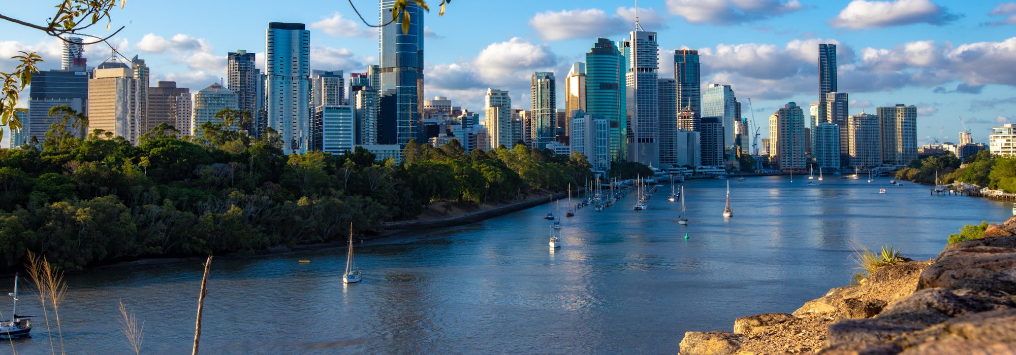 Bild på Brisbane med segelbåtar i vattnet, höghus och vacker natur.