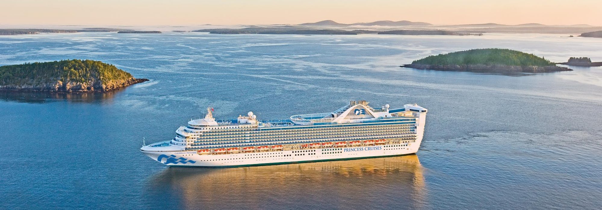 Fartyget Caribbean Princess glider fram i lugnt vatten mellan två gröna öar.
