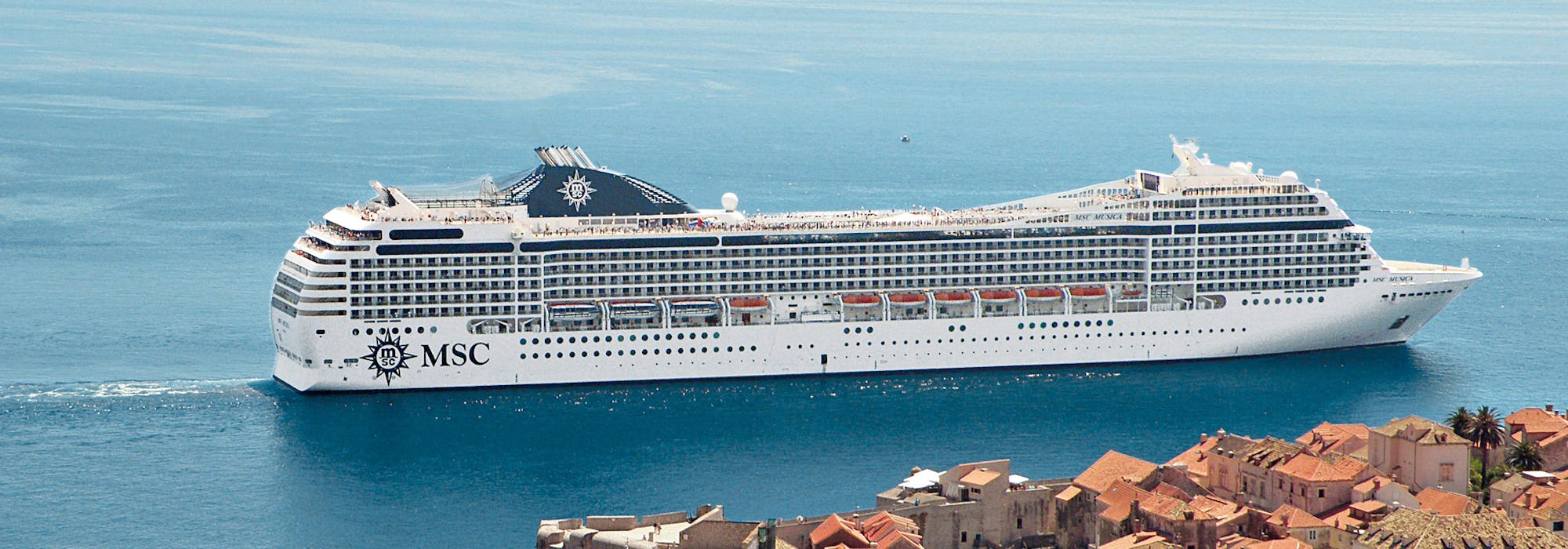 Bild tagen från sidan på MSC Musica som kryssar förbi en vacker hamn i Medelhavet.