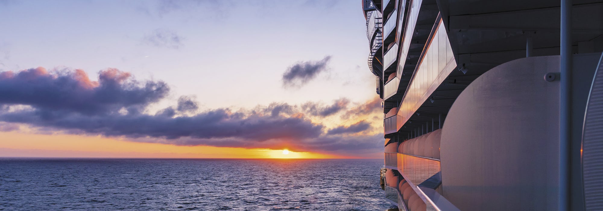Bild på sidan av fartyget Symphony of the Seas med havet och en vacker solnedgång i bakgrunden.