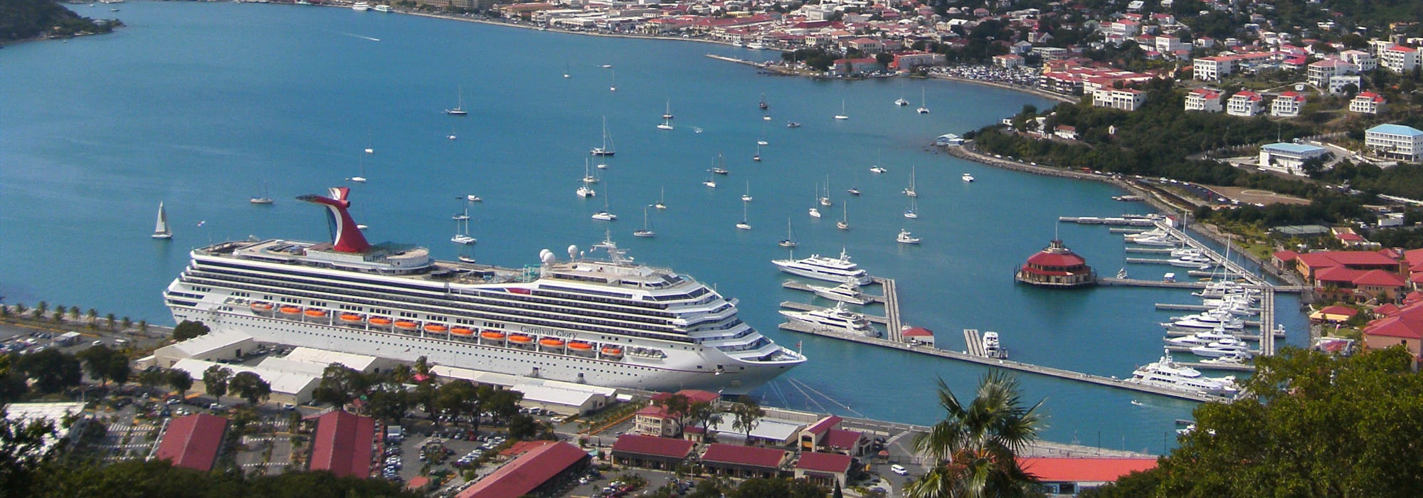 Carnival Glory ligger i hamn med höga berg och färgglada hus runtomkring.