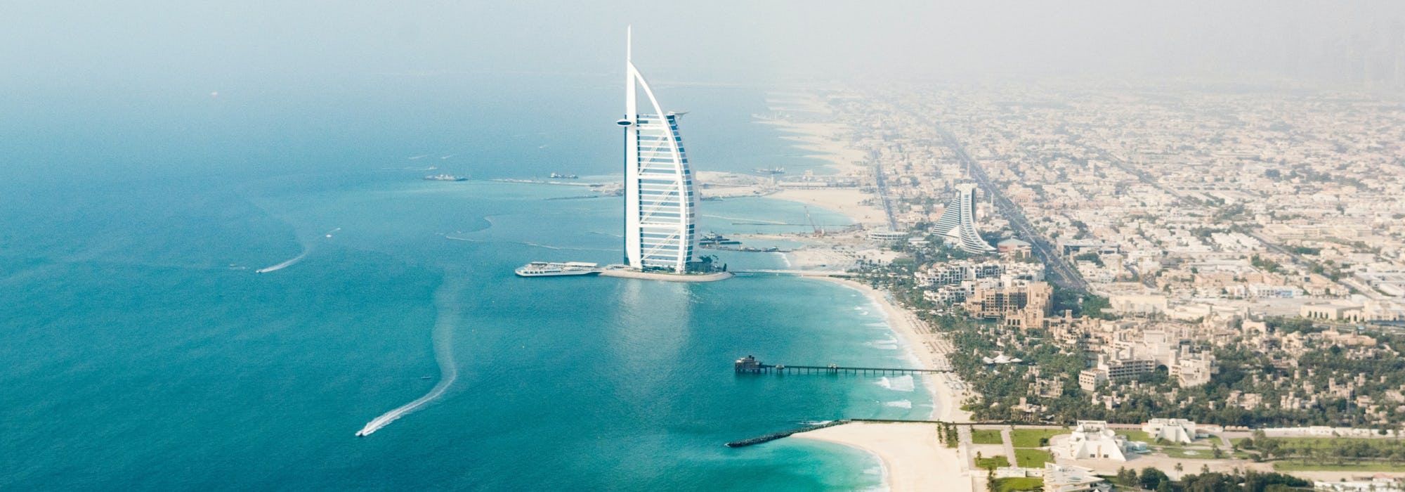 Överblicks bild över Dubais hamn med byggnader stränder och klarblått vatten.
