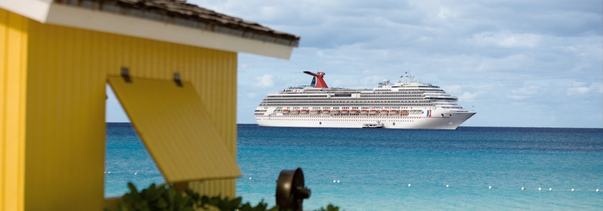 Carnival Splendor kryssar fram i ljusblått vatten bakom en guld byggnad.